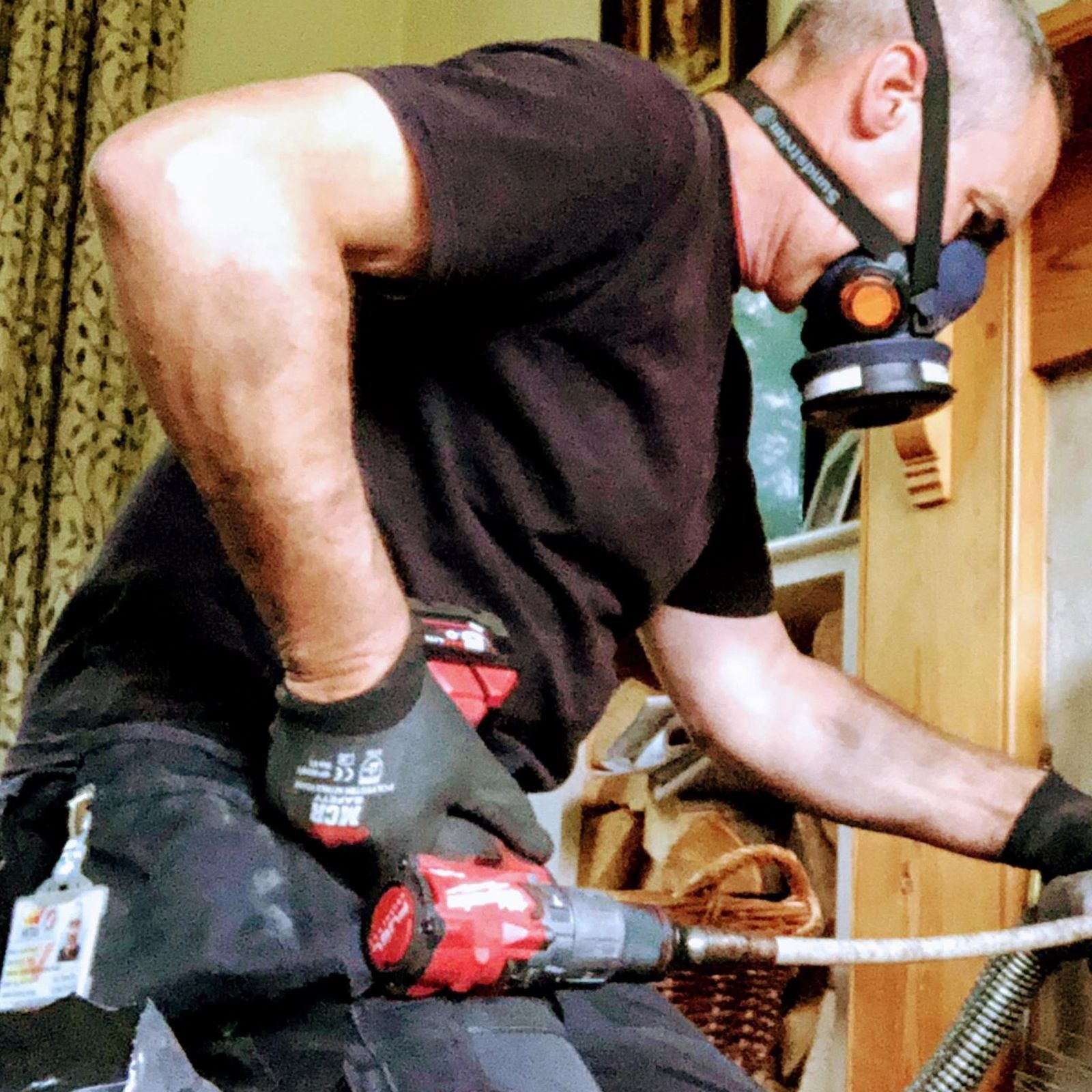 James at work indoors, wearing a respirator, with his sweeping rods and vacuum