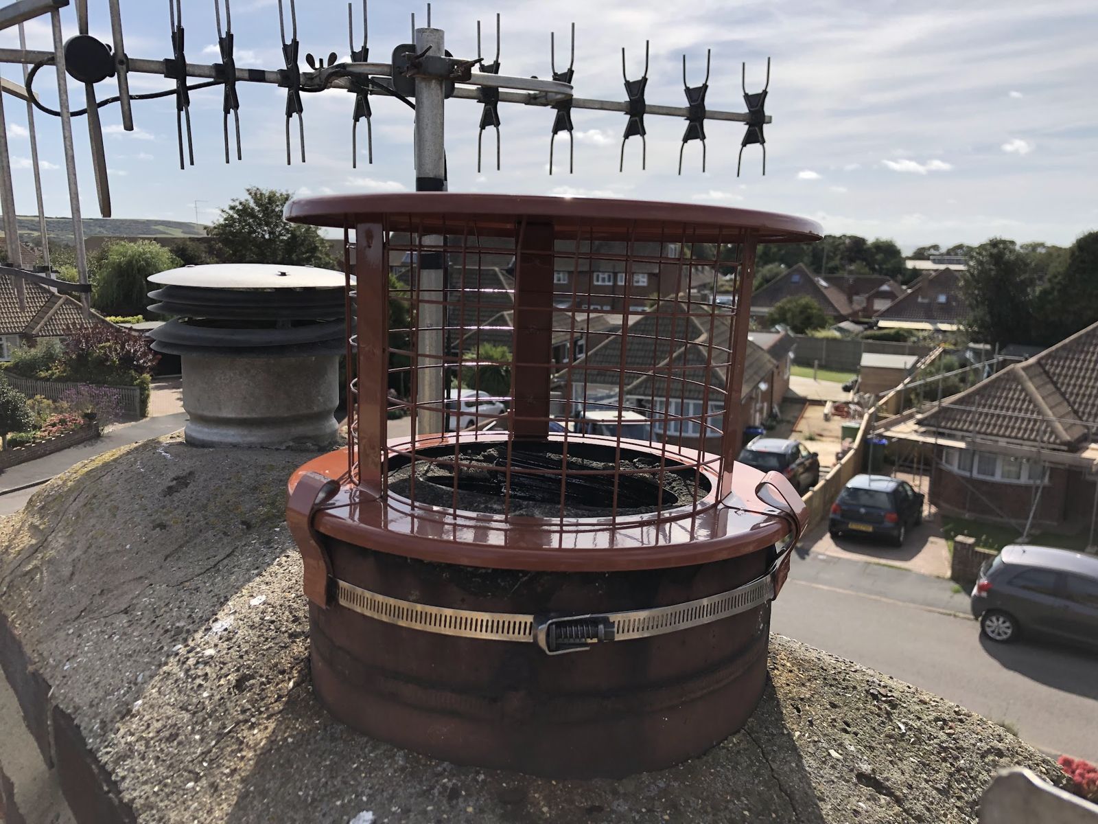 Terracotta bird guard cowl on a chimney with a TV aerial behind